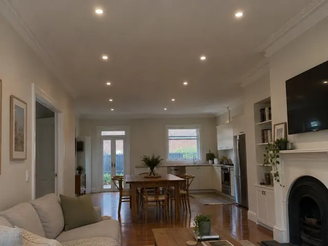 Living room and kitchen with recessed downlights in a cream interior, timber floors and fireplace in Waverley