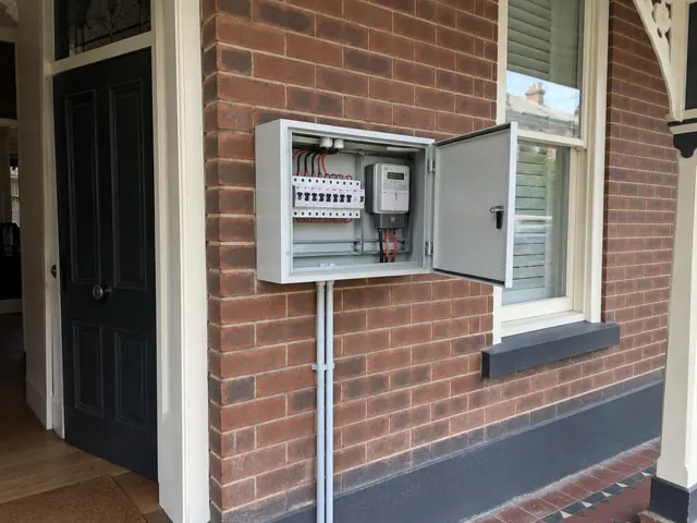 Open outdoor switchboard cabinet on a brick house wall beside a window in Randwick